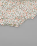 Detalle inferior de pelele bebé blanco con estampado floral rosa y verde, volante fruncido y broches verdes entreabiertos.