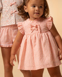 Vestido de bebé niña vichy rosa salmón con volantes en mangas y lazos decorativos al frente, estilo primavera verano