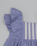 Detalle de vestido bebé niña en lino azul lavanda con volantes en hombro y entredoses de encaje blanco