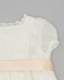 Vestido de bebé blanco en gazar con entredoses de encaje, mangas farol y lazo de raso rosa pastel en la cintura