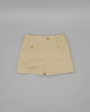 Bermuda infantil de sarga color beige con cintura elástica, bolsillos traseros con botones y cierre central.