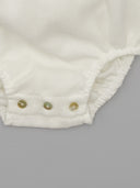 Detalle de entrepierna de pelele bebé blanco en gazar con tres botones nácar y acabado fruncido elástico.