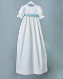 Vestido de comunión largo en piqué blanco roto con mangas abullonadas, encaje y fajín azul celeste.