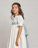 Vestido de comunión niña blanco roto con fajín de tul azul celeste, manga corta y detalles de encaje