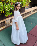 Vestido de comunión niña blanco largo en gazar con fajín rosa y corona de flores, manga 3/4 con smock