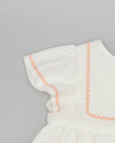 Detalle de manga volante de vestido infantil blanco en piqué con ribete ondulina rosa salmón