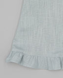 Detalle de bajo con volante fruncido de blusa de lino azul celeste claro con textura natural