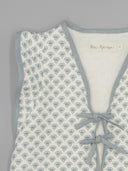 Chaleco acolchado infantil Fina Ejerique blanco con estampado floral azul, escote en V y lazos de cierre.