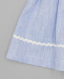 Detalle del bajo de falda azul celeste con cinta ondulina blanca decorativa y tela de algodón texturizado.