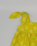 Vestido infantil amarillo con estampado de piñas, tirantes anudados y ribete ondulado en verde lima