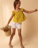 Short sarga blanco con bolsillos para niña, combinado con top amarillo estampado piñas y sandalias beige, look verano